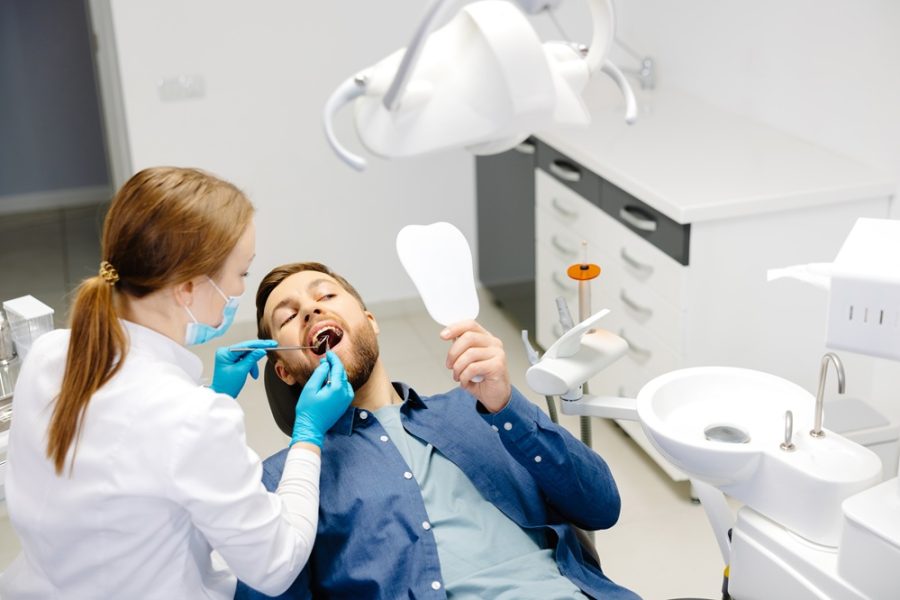 Dentist examining a patient’s teeth while the patient holds a mirror, helping detect early tooth decay symptoms during a routine dental visit – tooth decay symptoms