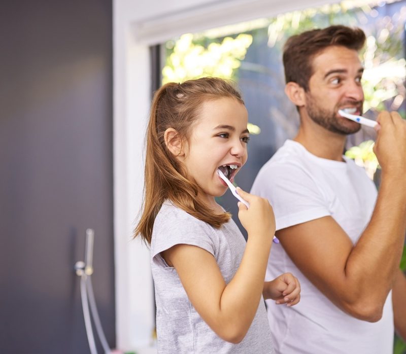 Father and daughter brushing their teeth together at home, demonstrating good oral hygiene habits recommended by bac decon dental – bac decon dental