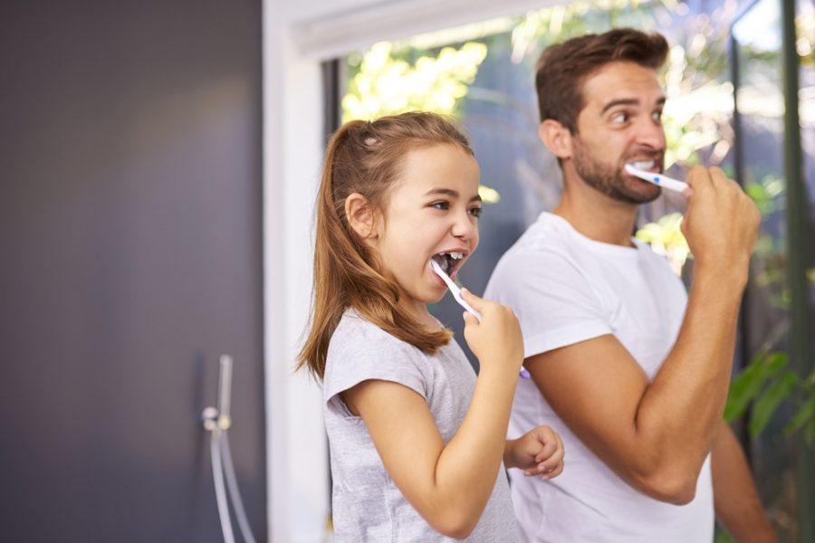 Father and daughter brushing their teeth together at home, demonstrating good oral hygiene habits recommended by bac decon dental – bac decon dental