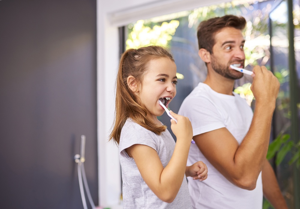 Father and daughter brushing their teeth together at home, demonstrating good oral hygiene habits recommended by bac decon dental – bac decon dental