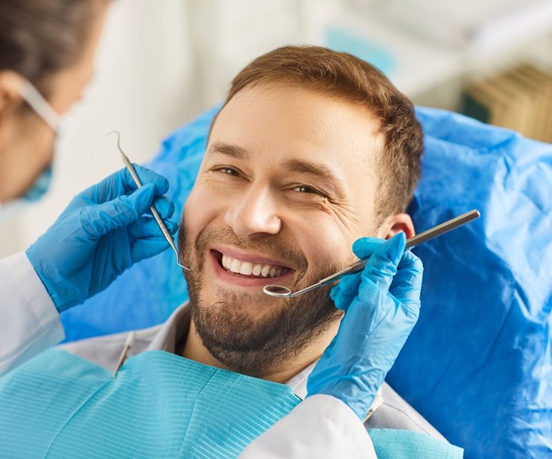 Patient smiling during a dental checkup while a dentist examines teeth and gums, highlighting preventive care for healty gums – healty gums