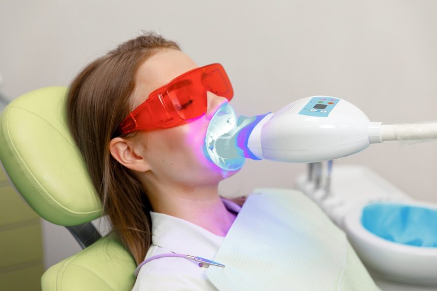 Patient undergoing professional teeth whitening with LED light and protective glasses at a dental clinic, illustrating treatment related to dental bleaching cost – dental bleaching cost